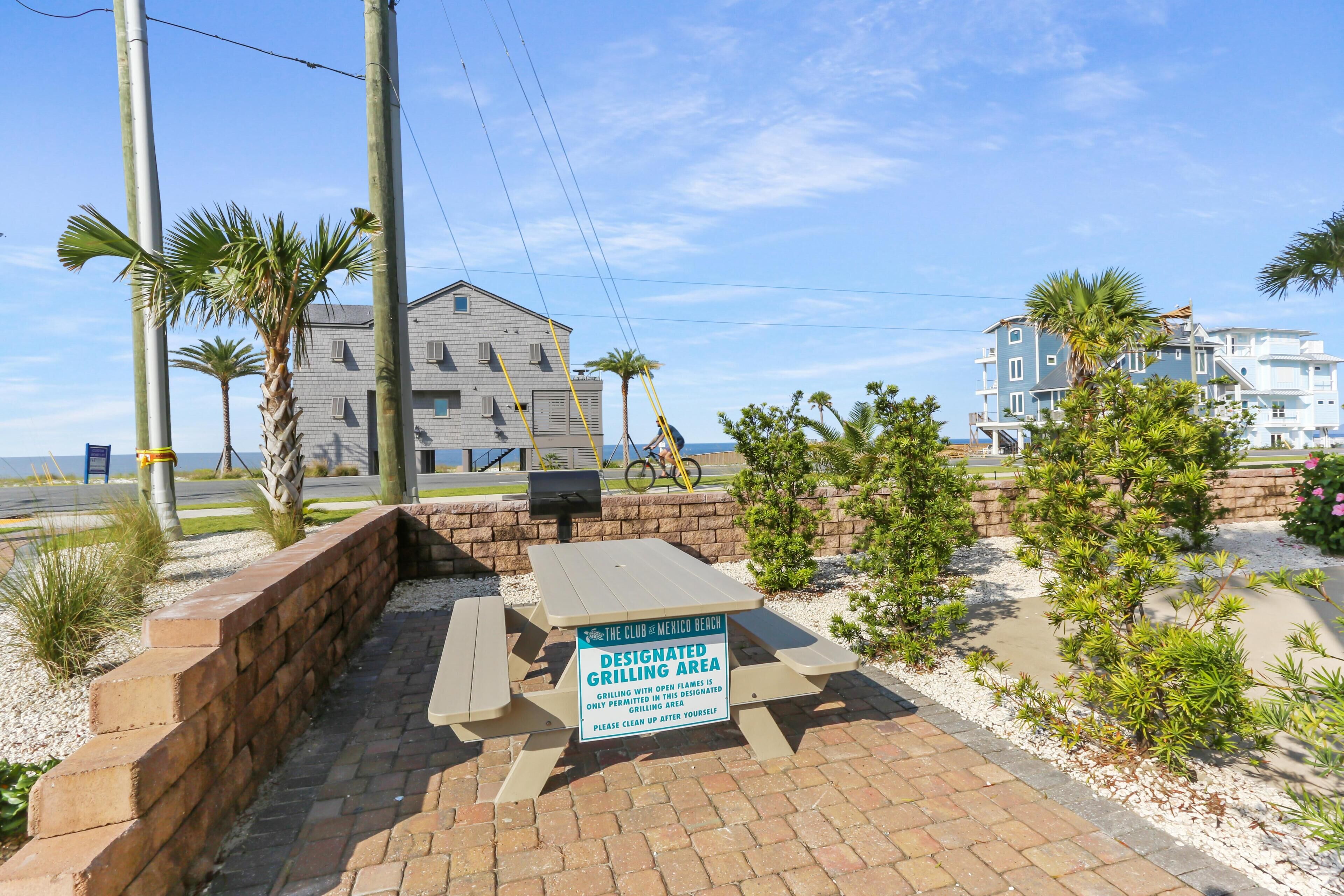 A designated grilling area with a sign, palm trees, and a building in the background.