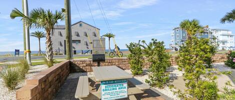A designated grilling area with a sign, palm trees, and a building in the background.