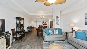 A spacious living room with a grey sofa, a coffee table, and a dining area with a wooden table and chairs. - Club at Mexico Beach 2C Coastal Dreaming (Port St. Joe)