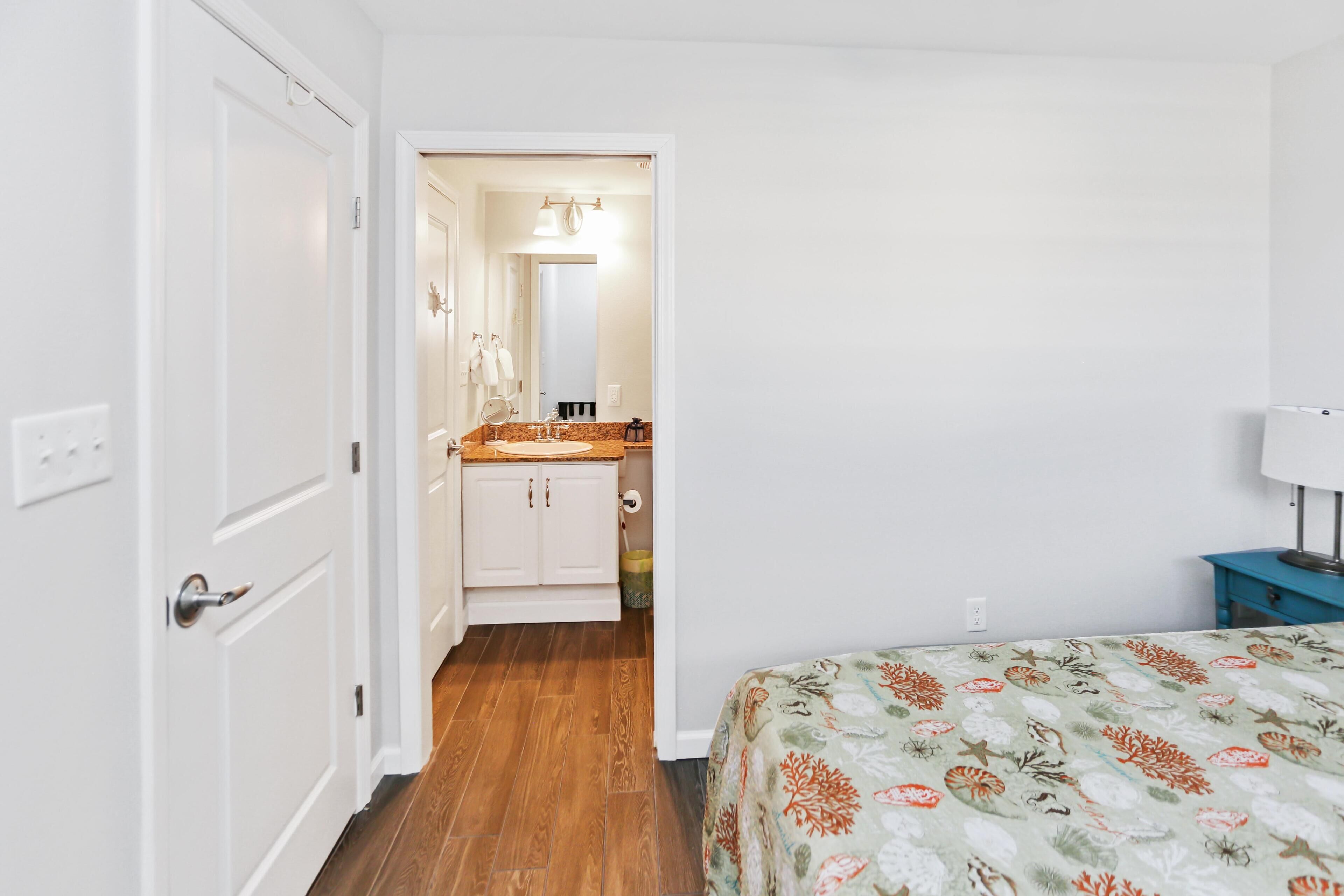 A bedroom with a bed, a nightstand, a dresser, and a bathroom visible through an open door.