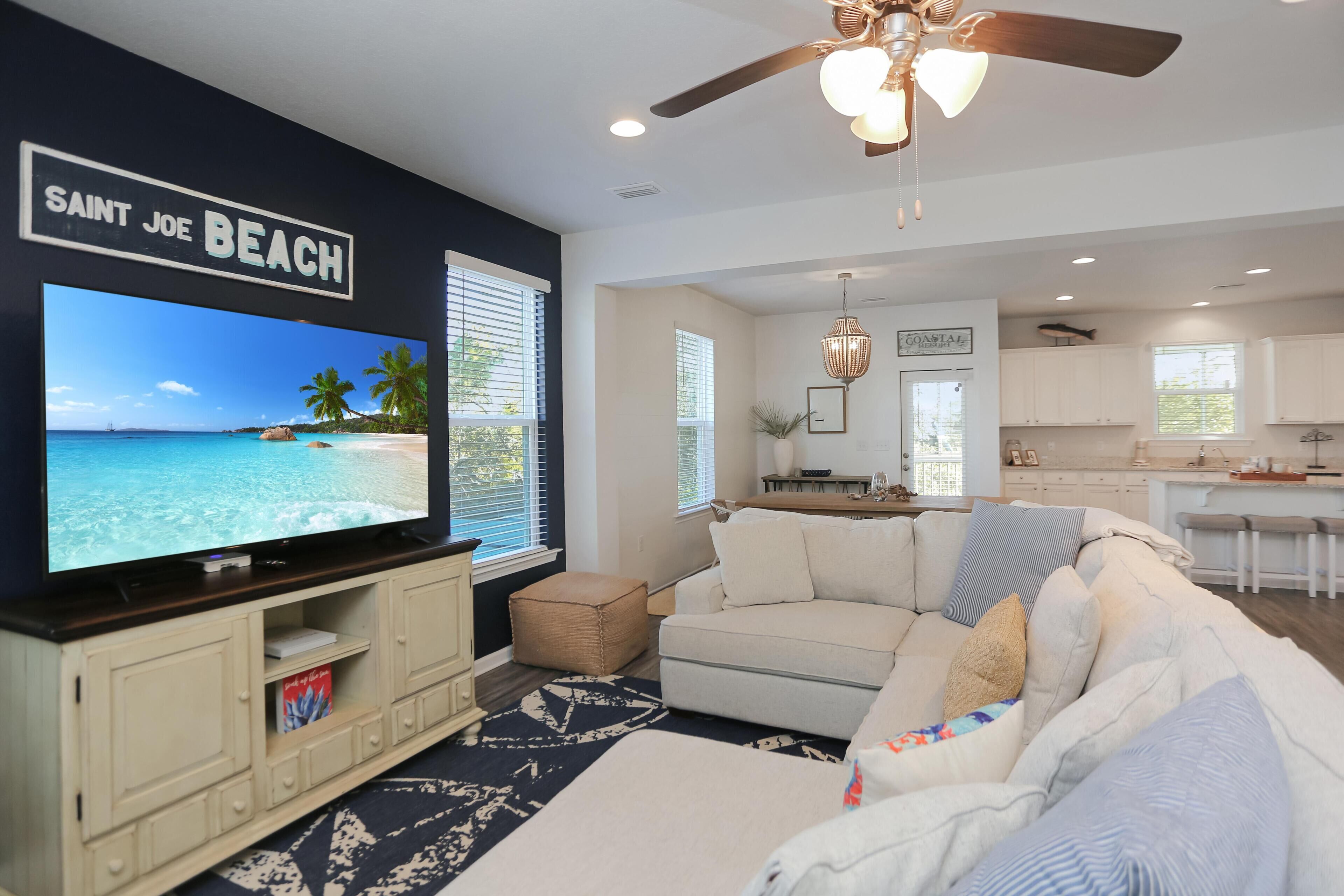 A living room with a large flat-screen TV, a white sofa, and a ceiling fan.