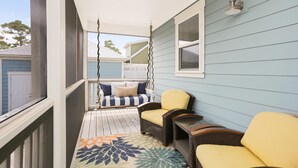 A covered porch with a swing chair, a cushioned bench, and a small table. - Song of the Sea (Port St. Joe)