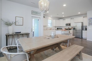 A modern kitchen with white cabinets, stainless steel appliances, and a wooden dining table with chairs. - Song of the Sea (Port St. Joe)
