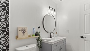 Une salle de bain comprenant des toilettes, un lavabo avec un miroir et une étagère avec des articles de toilette.