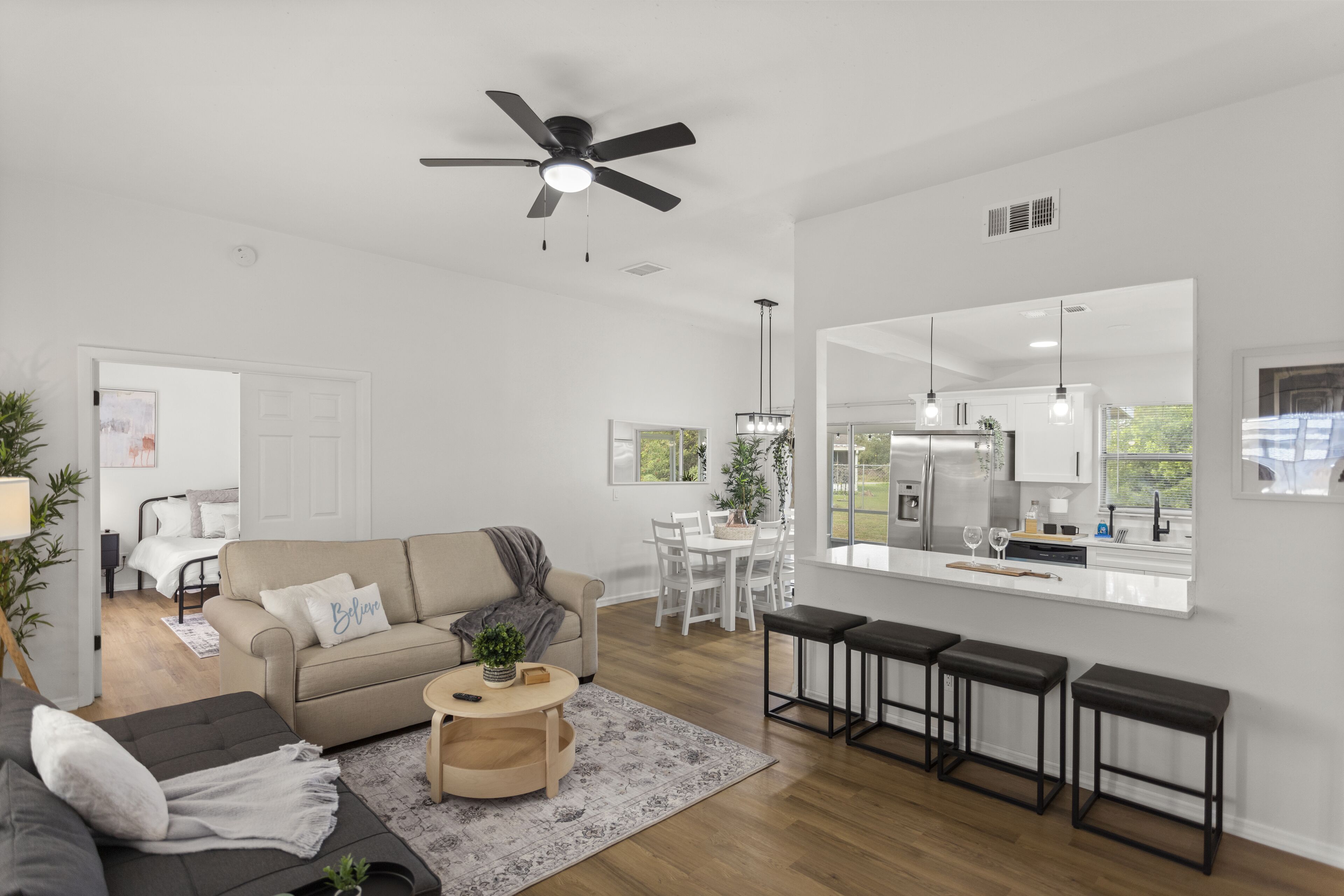 A modern living room with a beige sofa, a dark sofa, a coffee table, and a dining area with a white table and chairs.