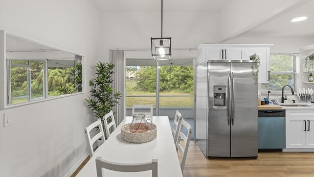Une cuisine moderne avec des meubles blancs, un réfrigérateur en acier inoxydable et un coin repas comprenant une table et des chaises blanches.