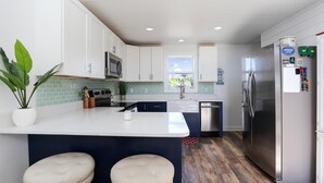 A modern kitchen with white cabinets, a stainless steel refrigerator, and a central island with two stools. - Eagle's Rest (Port St. Joe)