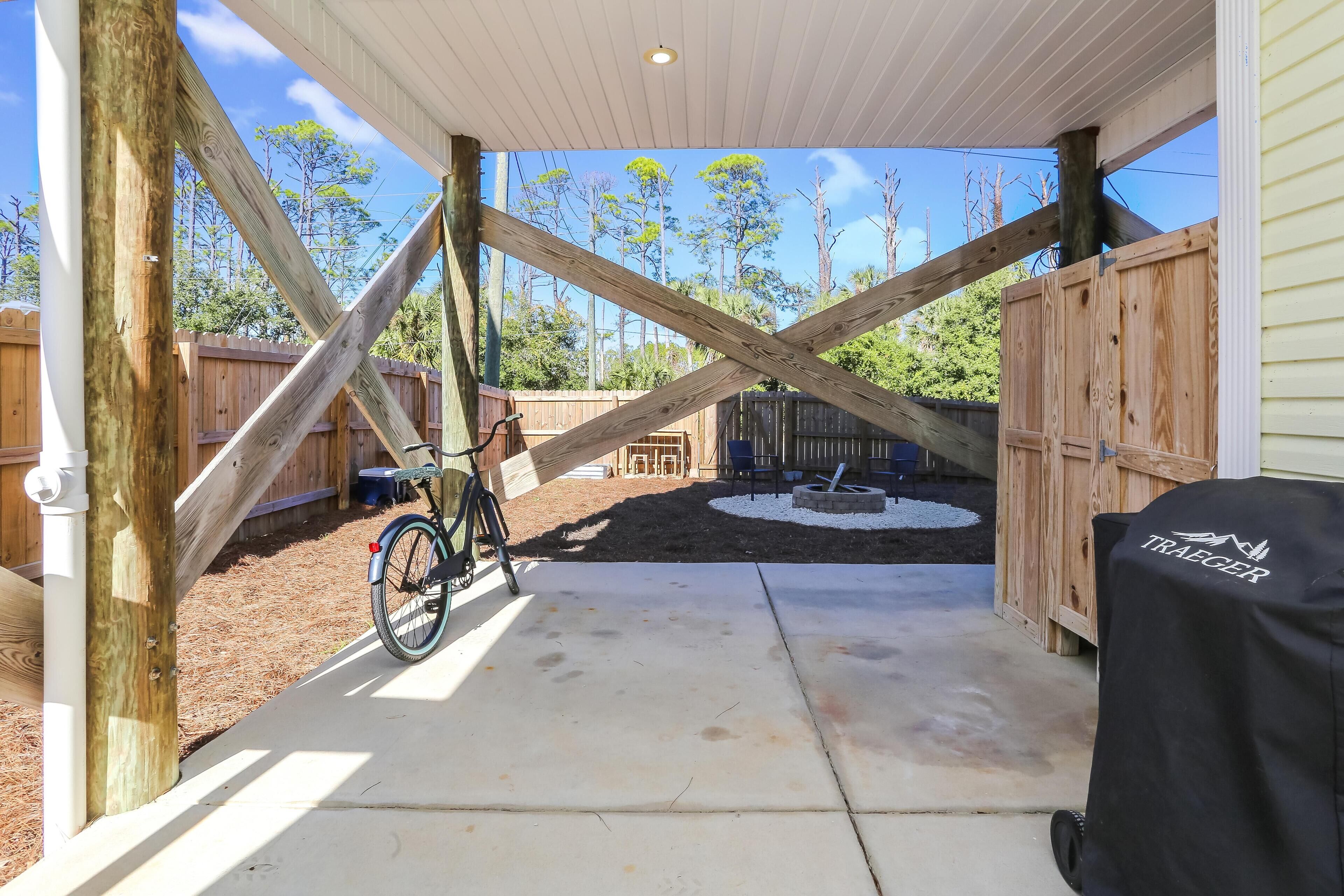 A covered patio area with a bicycle, wooden fence, and a grill cover.