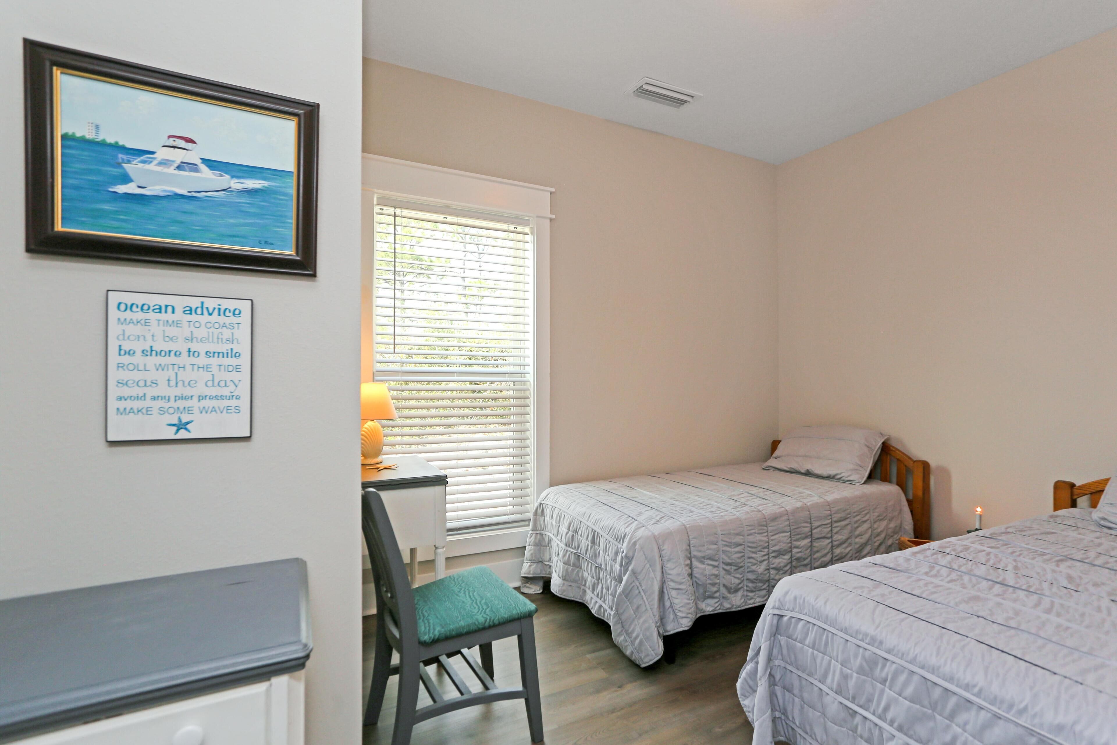A bedroom with two beds, a desk, a chair, and a window with blinds.