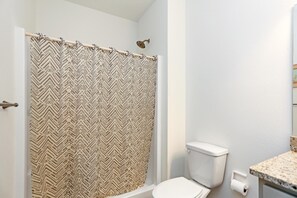Casa de banho com cortina de chuveiro, sanita e bancada.