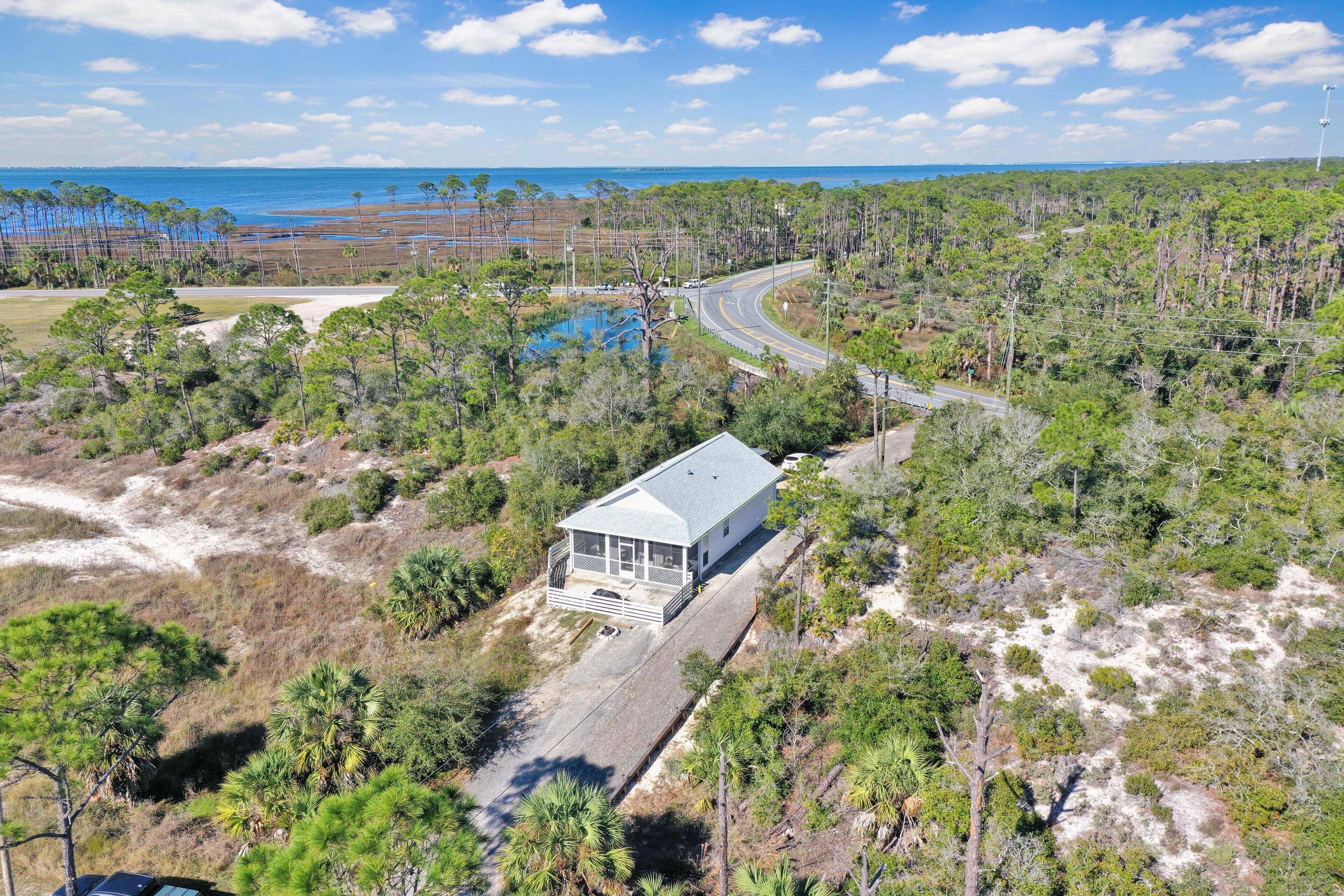 A coastal house with a large porch, surrounded by dense pine trees and a view of the ocean.