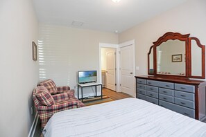 Quarto com uma cama, televisão sobre um suporte, cômoda e uma porta que dá para outro espaço.