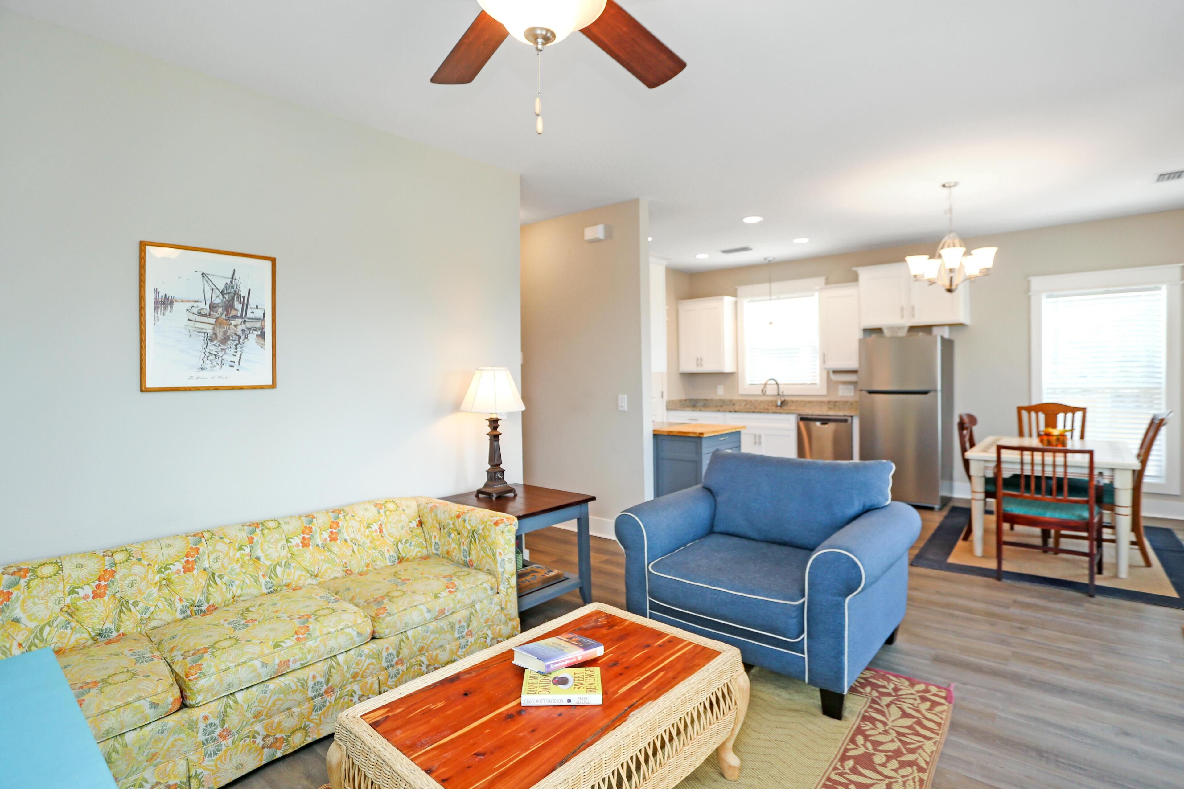 A living room with a floral sofa, a blue armchair, a wooden coffee table, and a dining area with a table and chairs.