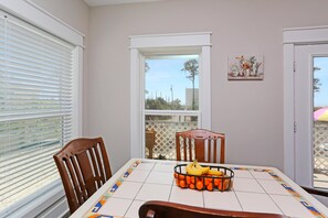 Uma área de jantar com uma mesa posta para dois, uma janela com persianas e vista para o exterior.