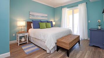 A bedroom with a bed, bedside tables, a bench, a ceiling fan, and a window with curtains.