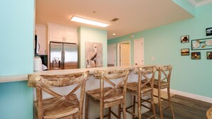 A kitchen with a bar area, wooden chairs, and a refrigerator. - Summerhouse 305 - Harvesting Sunshine II (Port St. Joe)