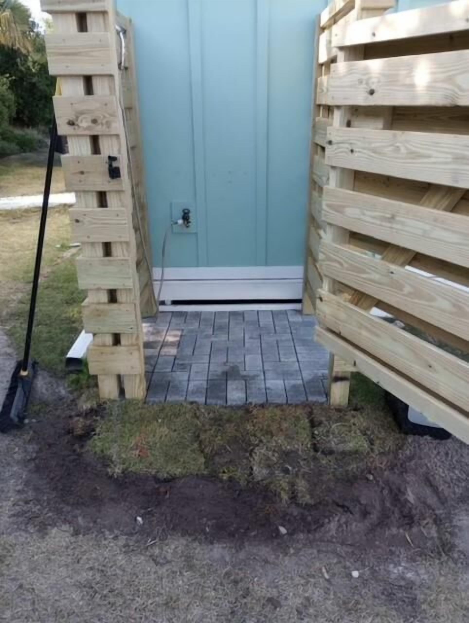 Une structure en bois dotée d’une porte, d’une marche menant à l’intérieur et d’une pelle posée sur le sol.