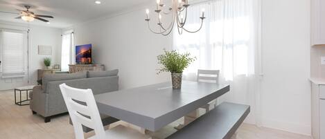 A modern dining area with a long table, benches, and a chandelier.