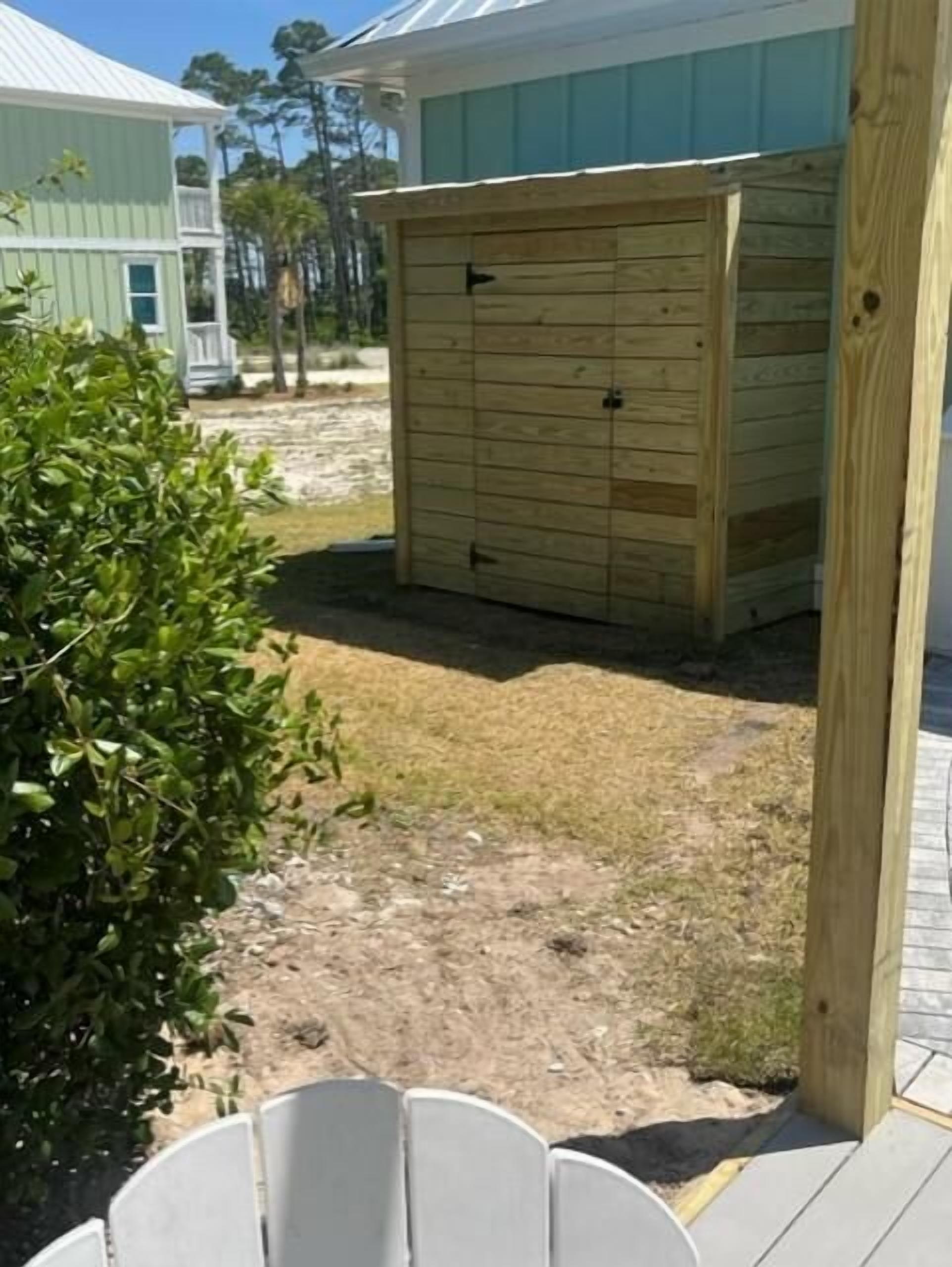 A wooden shed in a backyard with a dirt ground and a small bush.