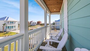 En inglasad veranda med vita Adirondack-stolar, ett träpanelat tak och utsikt över hus och strand.
