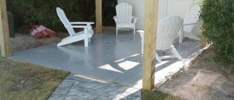 Un espacio de patio cubierto con una pérgola de madera, dos sillas Adirondack blancas y un sendero empedrado.
