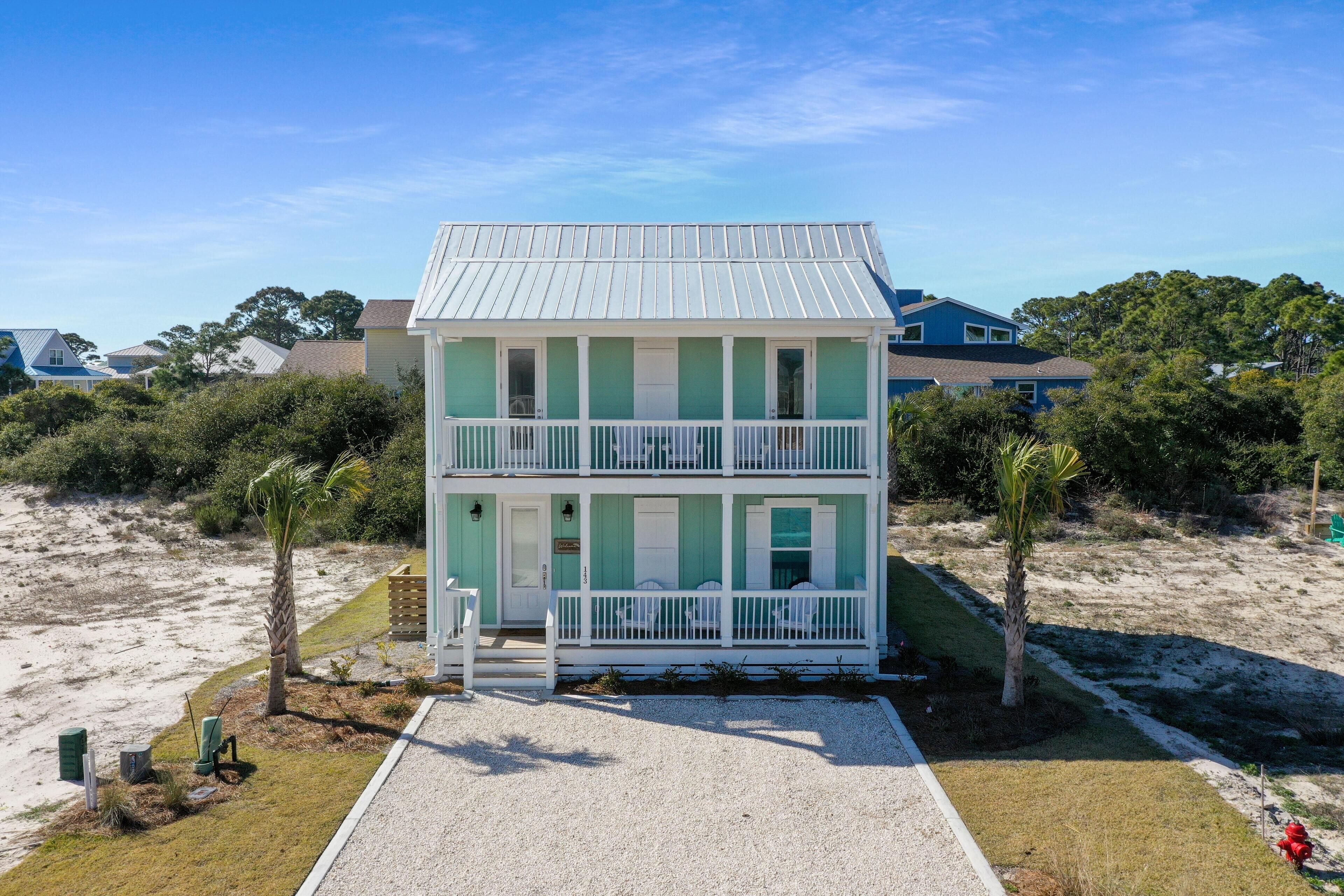 Ein zweistöckiges Strandhaus mit weißer Fassade und grünen Akzenten, ausgestattet mit einer Veranda und einem kleinen Deck.