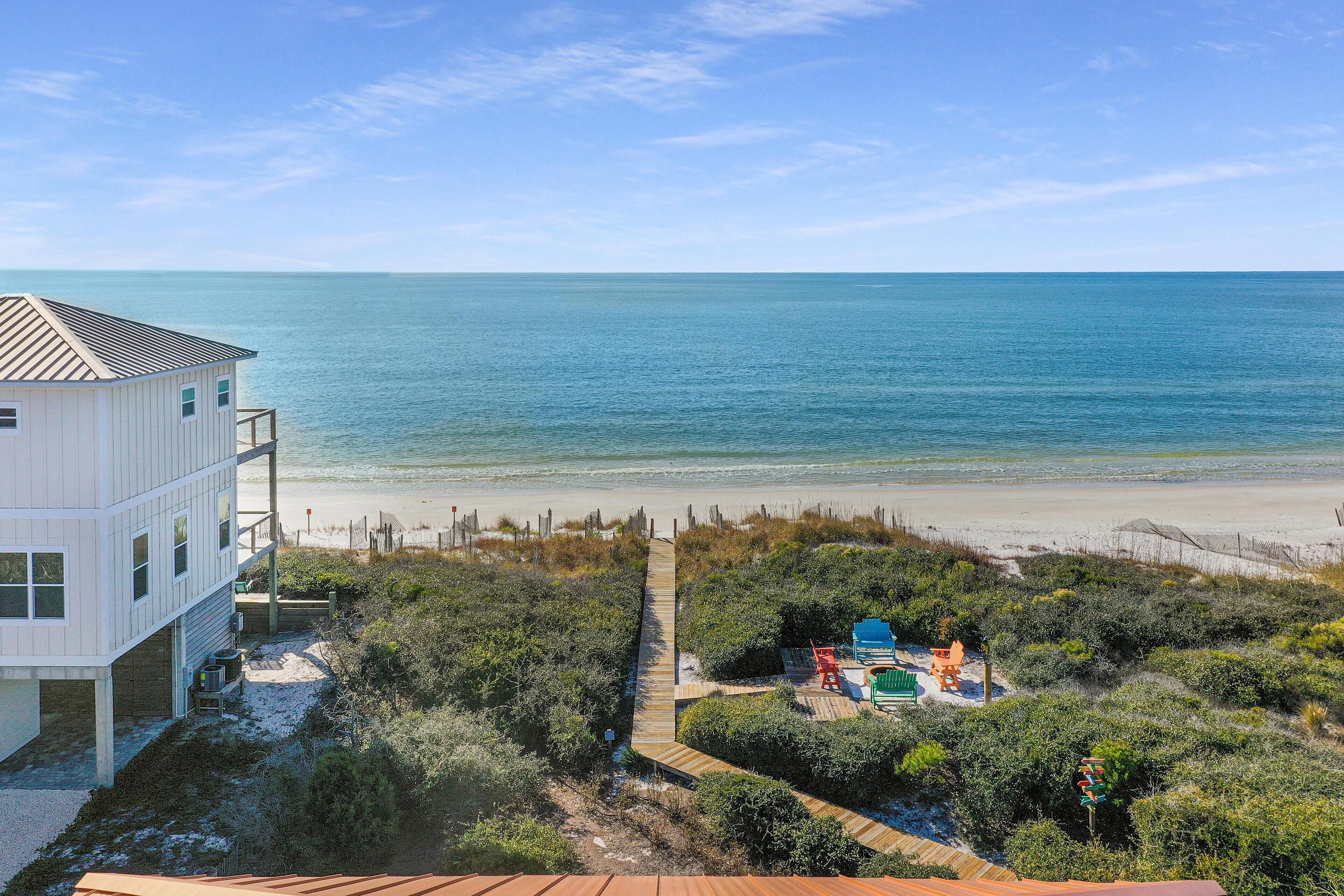 A beachfront property with a white building, a wooden deck, and beach chairs.