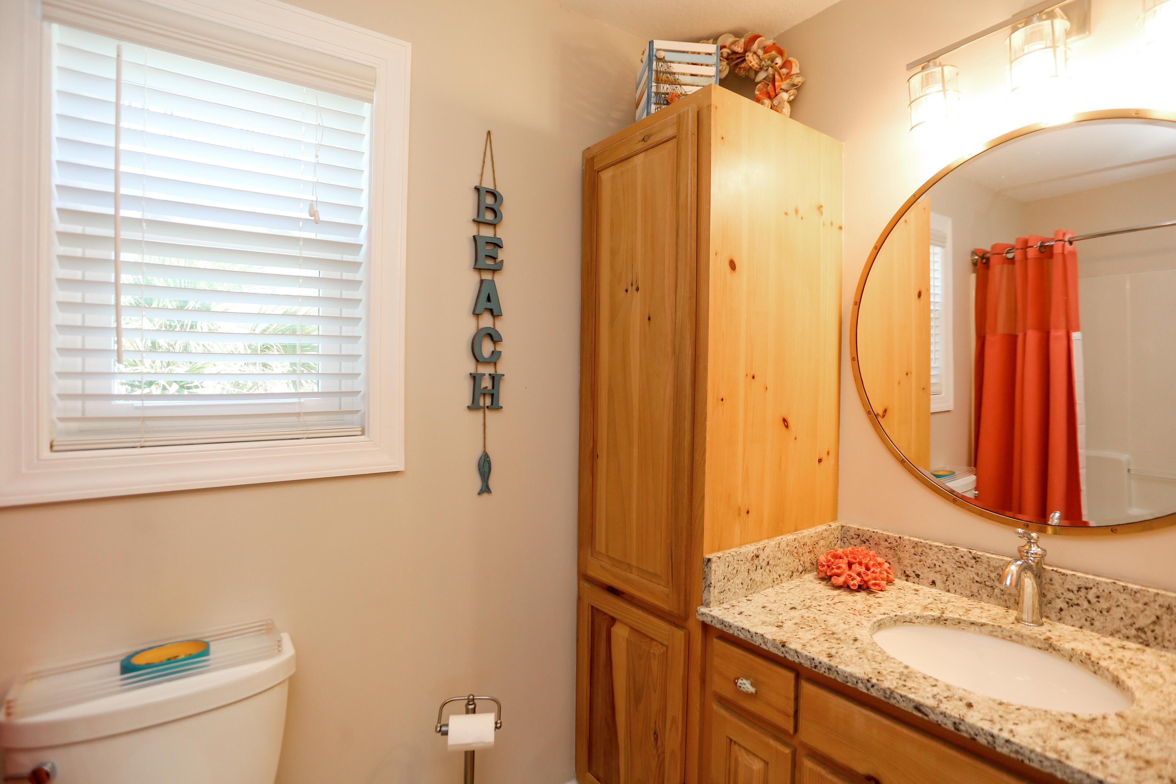 A bathroom with a toilet, sink, wooden cabinet, and a mirror.