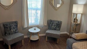 A room with two armchairs, a small round table, a window with blinds, and a mirror on the wall.