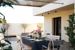 Un espace de restauration en plein air avec une table dressée pour un repas, entourée de chaises, et une pergola au-dessus.