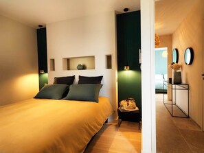 Une chambre à coucher avec un lit, des tables de chevet, un miroir et une vue sur une autre pièce.