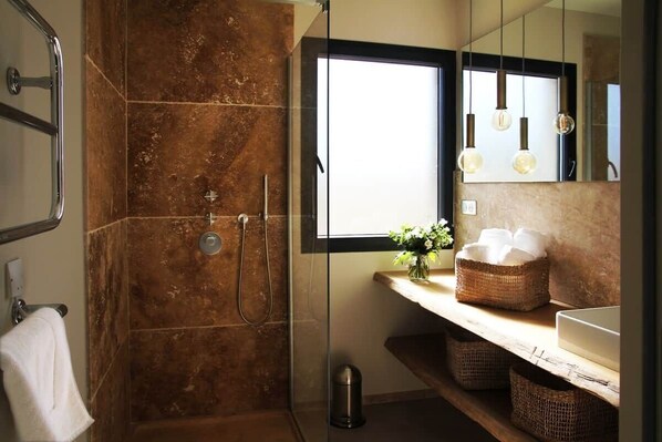 A bathroom with a glass-enclosed shower, a white sink, a mirror, and a window.