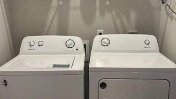 Due lavatrici a carica frontale affiancate, con ripiano sopra pieno di detersivi e accessori per la lavanderia.