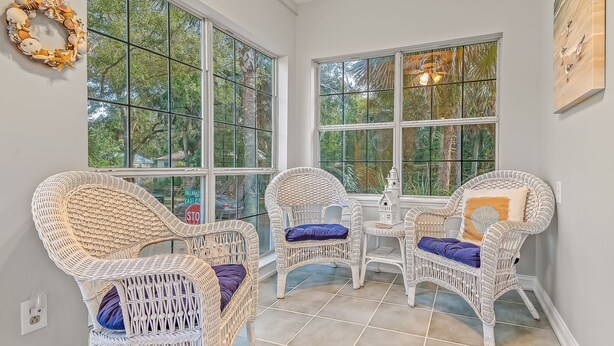 A sunlit room with large windows, wicker chairs with cushions, and a small table.