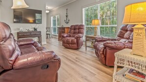 A spacious living room with leather sofas, a dining area, and large windows with green foliage.