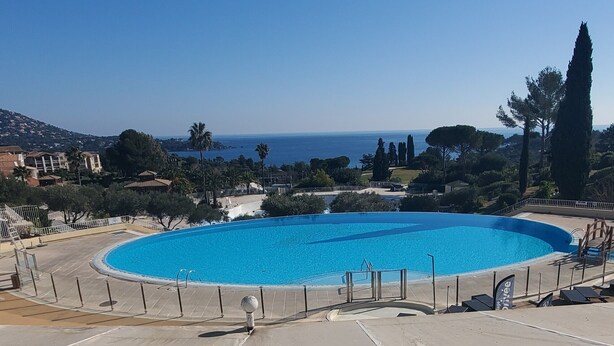 A circular pool with a clear blue poolside area, surrounded by a fence and various amenities. - Comfortable nest with pool and sea view (Saint-Raphaël)