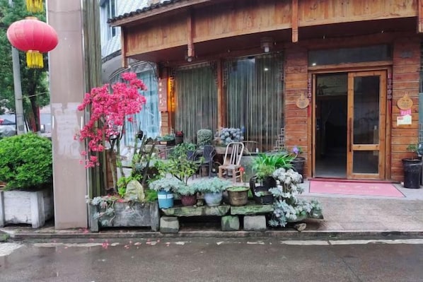 A traditional wooden building with a wooden porch, potted plants, and a red lantern.