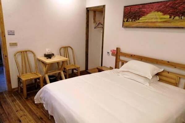 A bedroom with a bed, two wooden chairs, a small table, a mirror, and a painting on the wall.