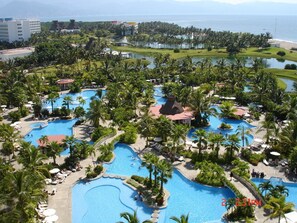 Ein Resort mit mehreren Schwimmbecken, umgeben von Palmen und Blick auf den Ozean.