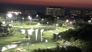Ein Golfplatz im Abenddämmerung mit beleuchteten Lichtern, Wasserspielen und umliegender Bepflanzung.