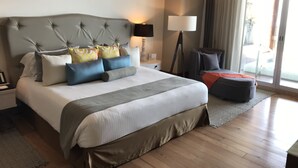Ein Hotelzimmer mit einem großen Bett, einem Nachttisch, einer Lampe, einem Sessel und Blick ins Freie.