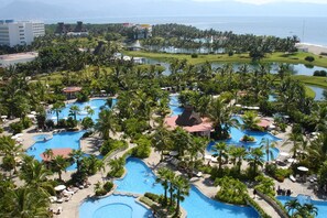 Een resort met meerdere zwembaden, omringd door palmbomen en uitzicht op de oceaan.