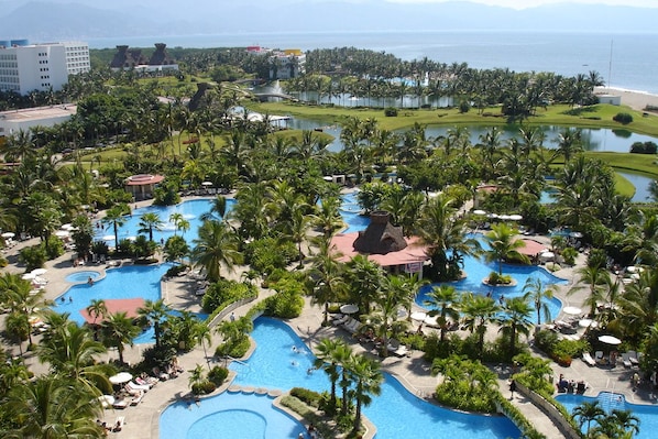 Un resort con varias piscinas rodeadas de palmeras y vistas al océano.