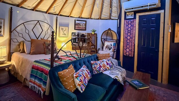 Interior d'una iurta amb un llit, una cadira, una taula i una porta.