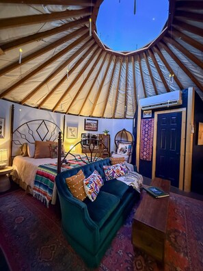 A yurt interior with a bed, a chair, a table, and a door. - Glamp in Heated Yurt in Big Bend @ Casa de Marca (Alpine)