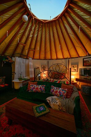 A cozy interior with a curved ceiling, a green sofa, a wooden coffee table, and a bed with a metal frame. - Glamp in Heated Yurt in Big Bend @ Casa de Marca (Alpine)