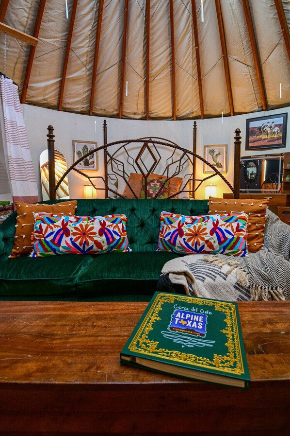 A cozy interior with a green sofa, colorful pillows, a wooden coffee table with a book, and a metal bed frame.