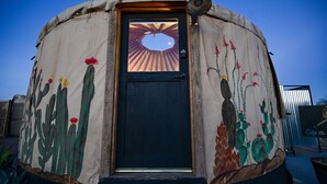 Una estructura circular amb una porta, amb un mural de paisatge desèrtic i una vista del capvespre a través de la porta.