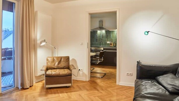 A modern living room with a leather armchair, a dining area, and a kitchen visible through an open door. - Air-conditioned apartment with balcony - Deidesheim (Deidesheim)