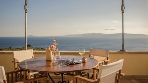 A round table with chairs, a glass of wine, a book, and a vase with flowers. - Villa Comi (Kefalonia)